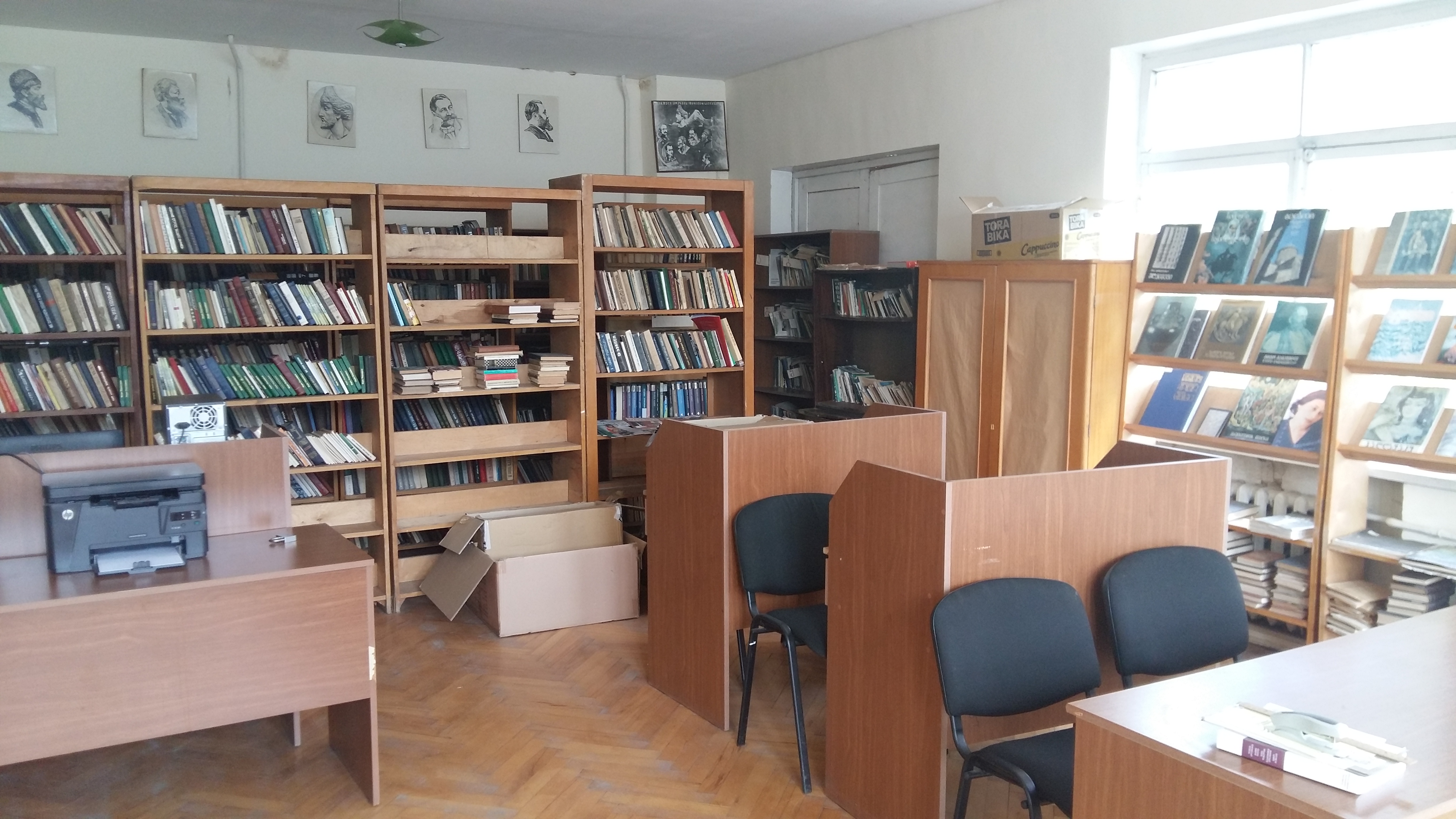 The stacks in the public library in Jokolo, with some desks and a computer in the foreground.