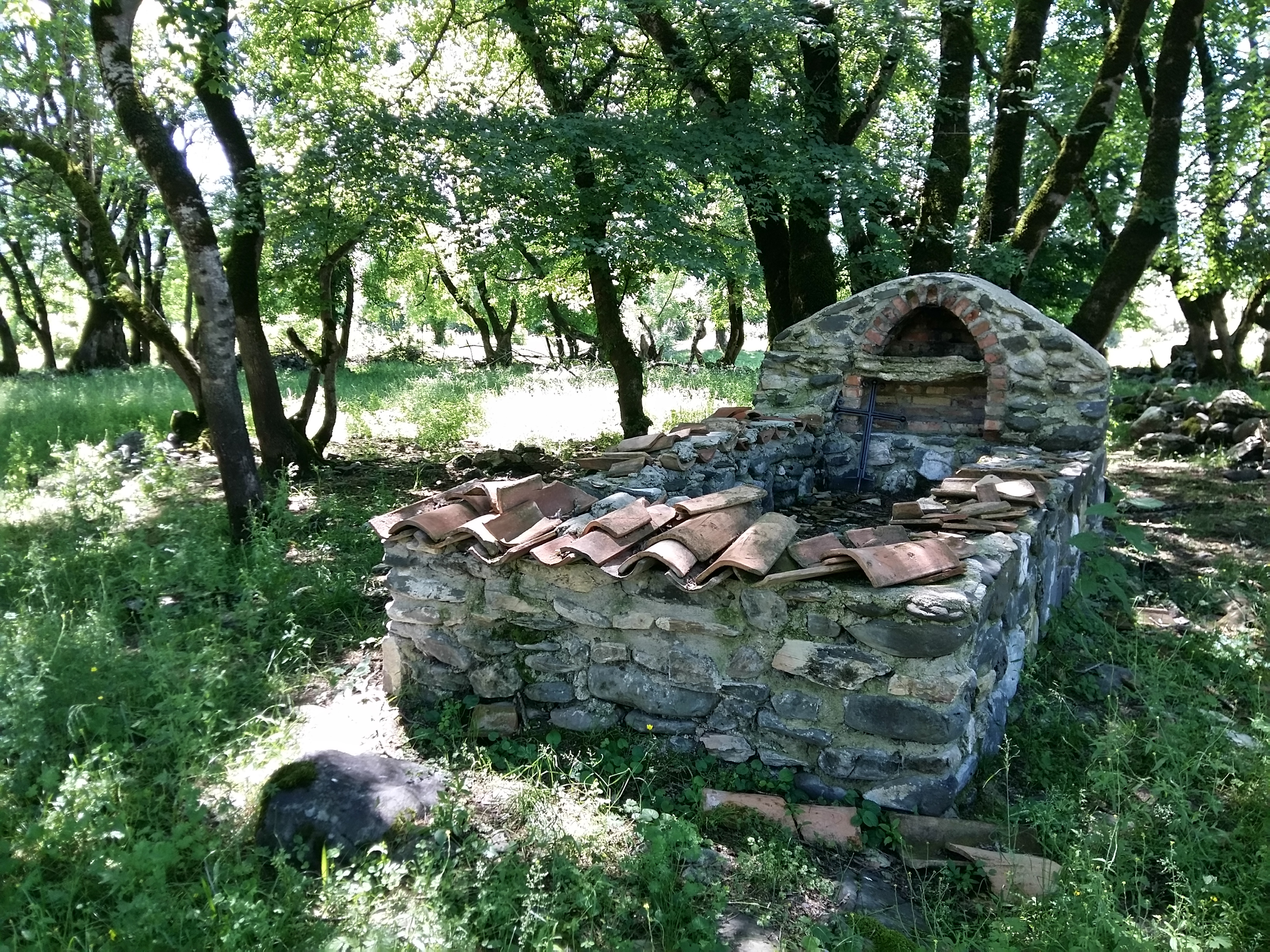 Low rectangular stone structure in a grove of trees.