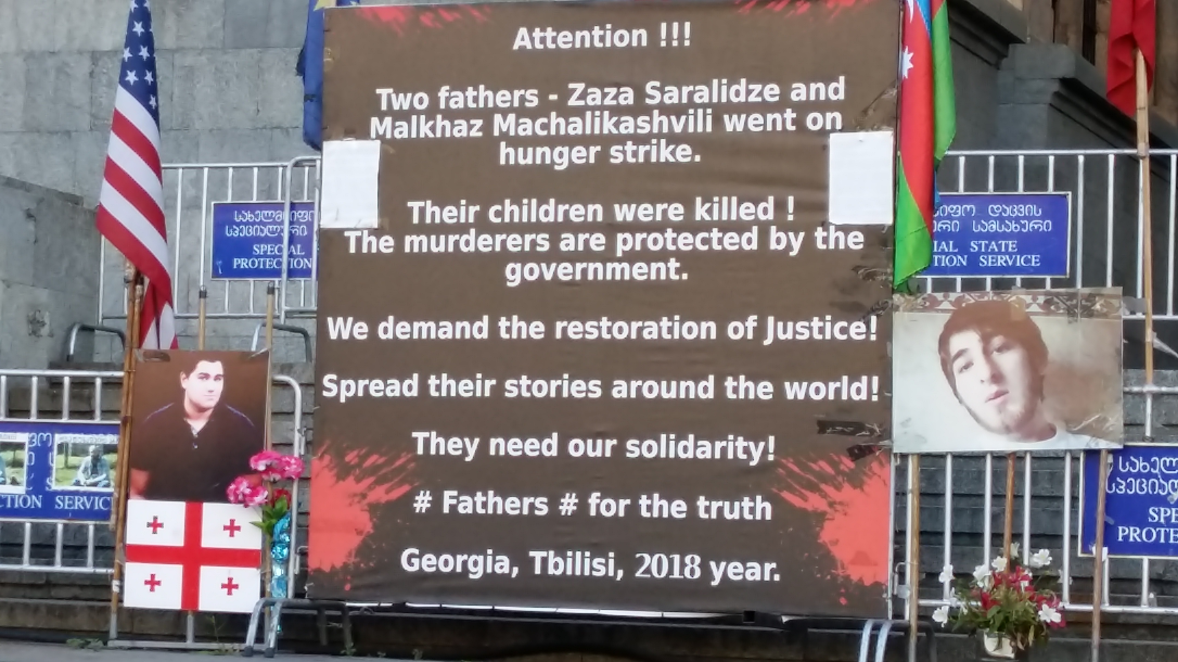 The sign says "Attention!!! Two fathers - Zaza Saralidze and Malkhaz Machalikashvili went on hunger strike. Their children were killed! The murderers are protected by the government. We demand the restoration of justice! Spread their stories around the world! They need our solidarity! # Fathers # for the truth. Georgia, Tbilisi, 2018 year."