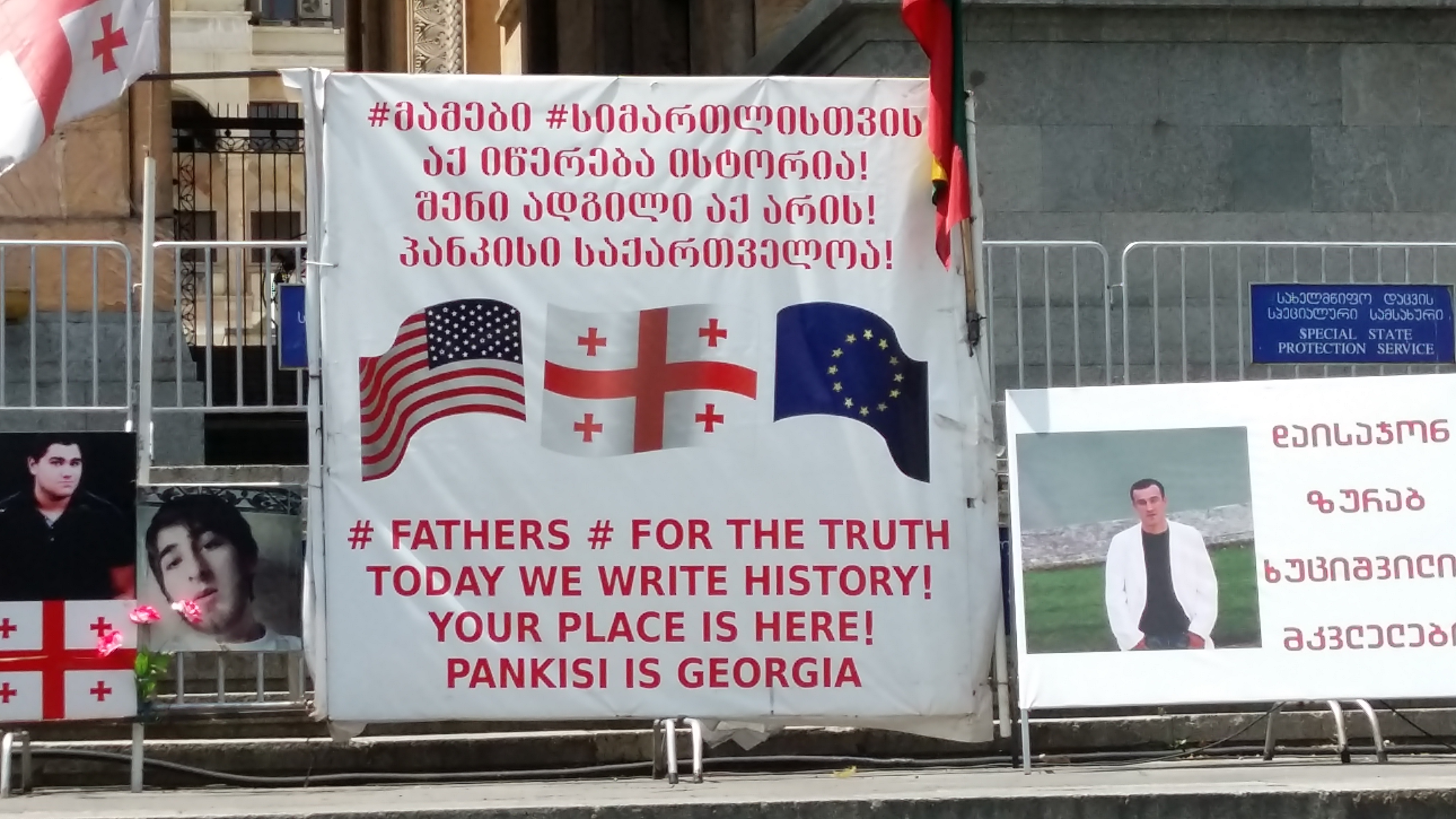 The sign says "# FATHERS # FOR THE TRUTH / TODAY WE WRITE HISTORY! YOUR PLACE IS HERE! PANKISI IS GEORGIA" in Georgian and English, together with the flags of the US, Georgia and the EU.