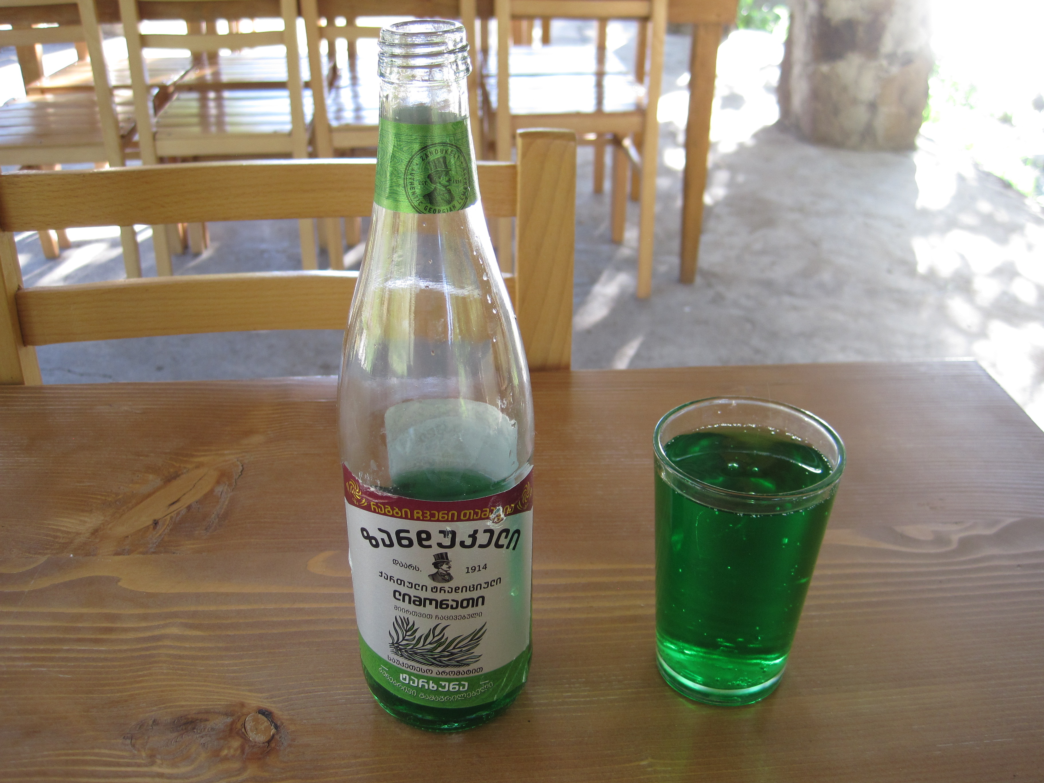A bottle and glass of bright green tarragon limonadi.