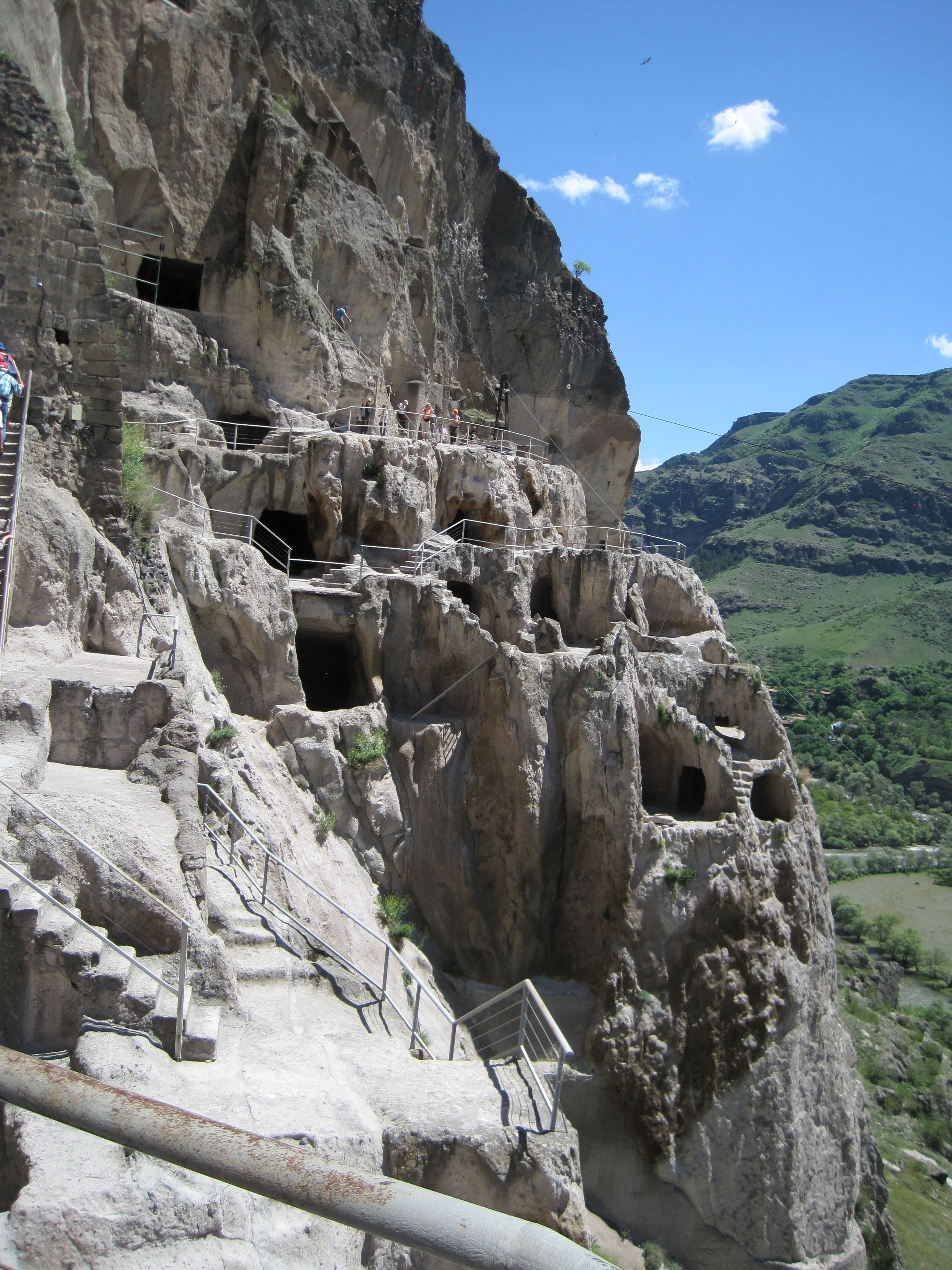 Caves entrances with stairways carved between them, and a steep drop to the valley floor below.