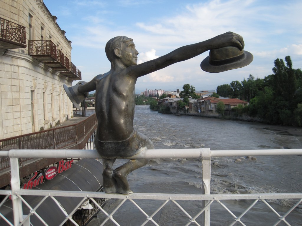 Sculpture of a boy sitting on the rail of a bridge stealing hats and dropping them in the river. White Bridge, Kutaisi.