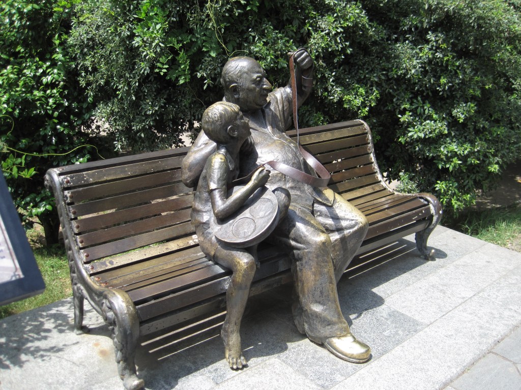 Sculpture of a man and boy sitting on a park bench, looking at a reel of film, Kutaisi.