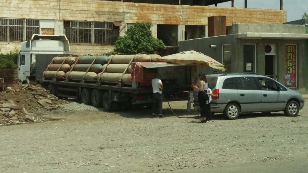 Woman and child filling up a minivan with gas from an ad hoc gas station consisting of a flatbed truck loaded with cylinders of compressed natural gas.