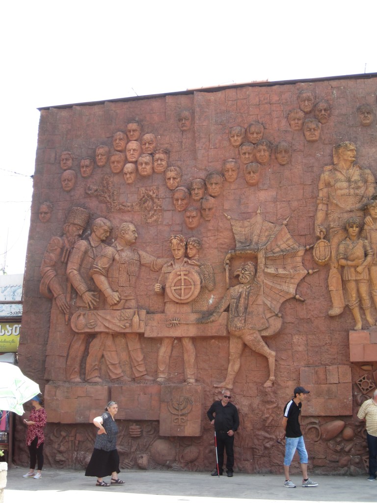 Relief sculpture on the wall of the Green Bazaar in Kutaisi, Georgia, featuring workmen, men's faces, and a devil (?).